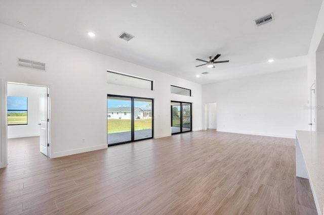 unfurnished living room featuring ceiling fan, light hardwood / wood-style flooring, and a towering ceiling