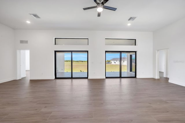 spare room with ceiling fan, a towering ceiling, and light wood-type flooring