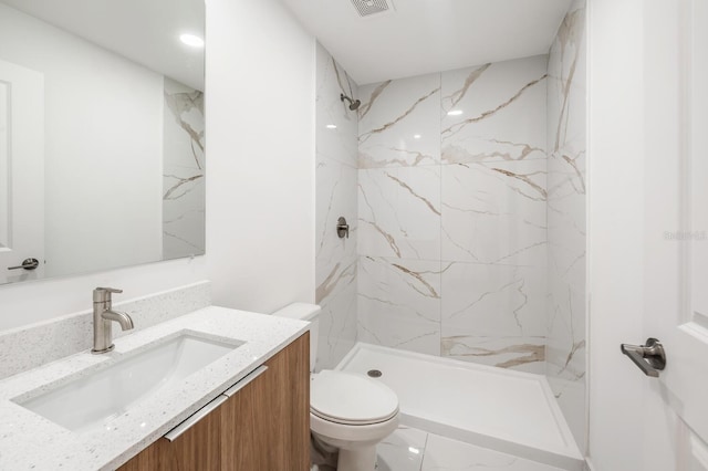 bathroom with vanity, tiled shower, and toilet