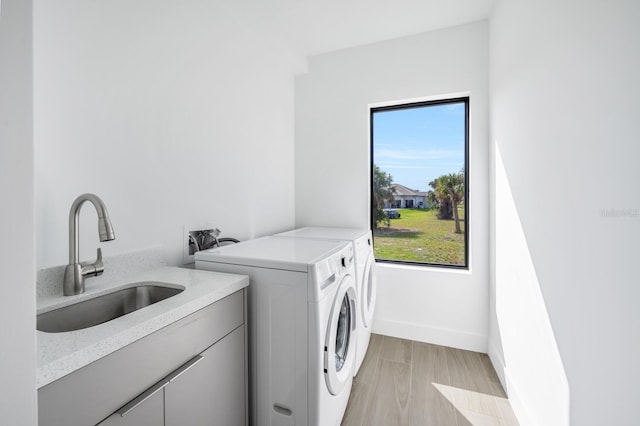 laundry area with cabinets, sink, washer and clothes dryer, and light hardwood / wood-style flooring