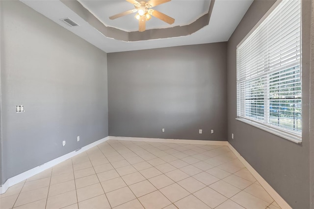 tiled spare room with a wealth of natural light, a raised ceiling, and ceiling fan