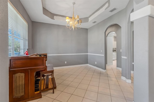 tiled empty room with an inviting chandelier and a raised ceiling