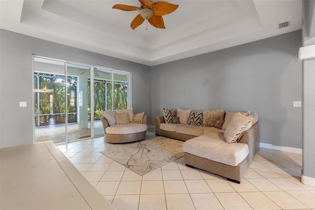 tiled living room with a tray ceiling and ceiling fan