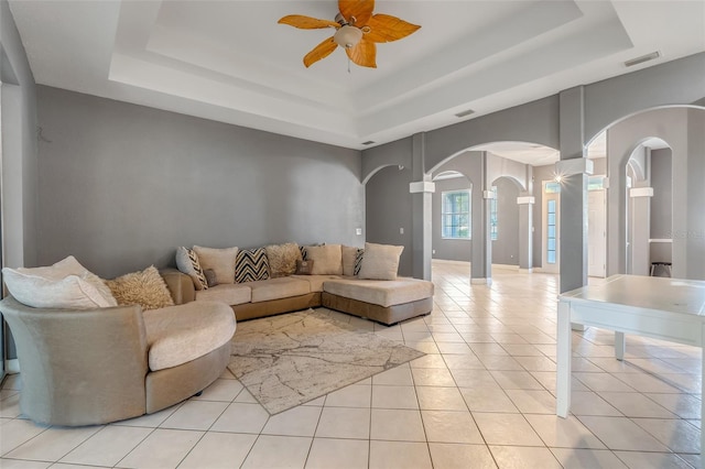 tiled living room with decorative columns, ceiling fan, and a raised ceiling