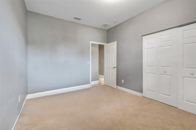 unfurnished bedroom featuring a closet, a textured ceiling, and light colored carpet