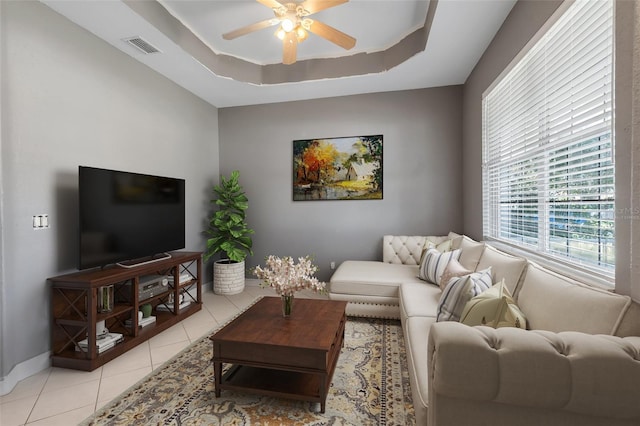 living room with ceiling fan, a tray ceiling, and light tile patterned floors