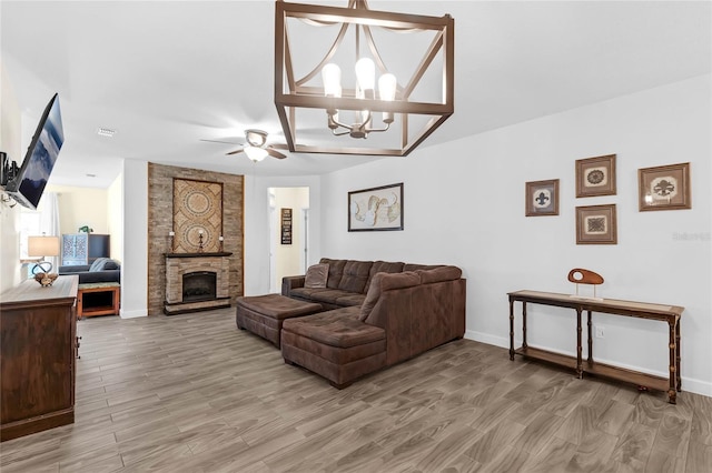 living room with ceiling fan with notable chandelier, a fireplace, and hardwood / wood-style floors