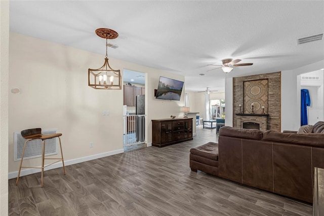 living room featuring hardwood / wood-style flooring, a textured ceiling, a brick fireplace, and ceiling fan with notable chandelier