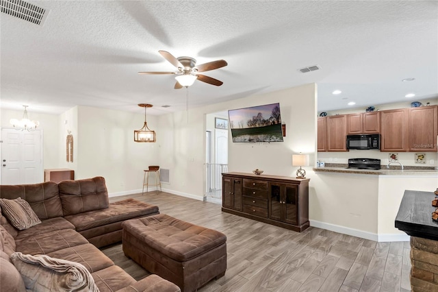 living room with ceiling fan with notable chandelier, a textured ceiling, and light wood-type flooring