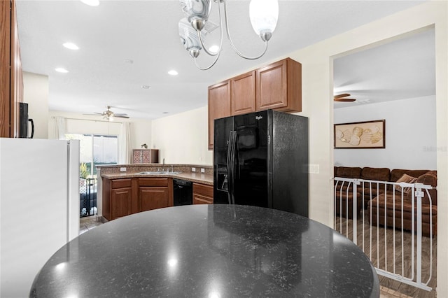 kitchen with sink, black appliances, ceiling fan with notable chandelier, and dark stone counters