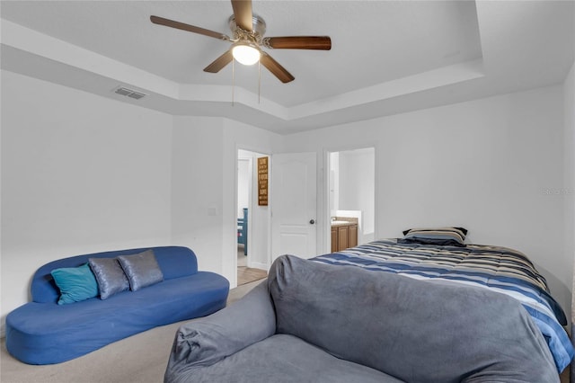 bedroom featuring carpet floors, ensuite bathroom, a tray ceiling, and ceiling fan