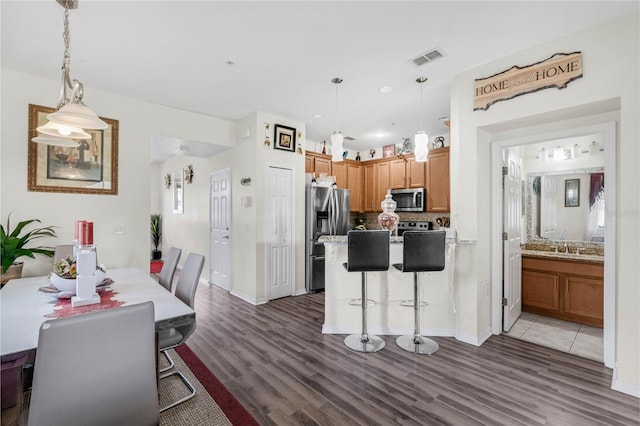 kitchen with a kitchen breakfast bar, decorative light fixtures, stainless steel appliances, and dark hardwood / wood-style flooring