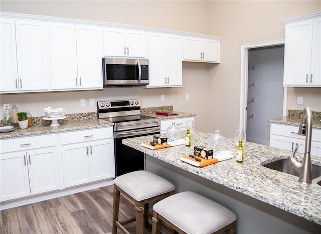 kitchen with appliances with stainless steel finishes, white cabinetry, a kitchen bar, light wood-type flooring, and sink