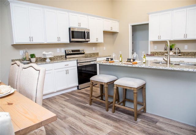 kitchen with sink, white cabinetry, stainless steel appliances, and light hardwood / wood-style floors