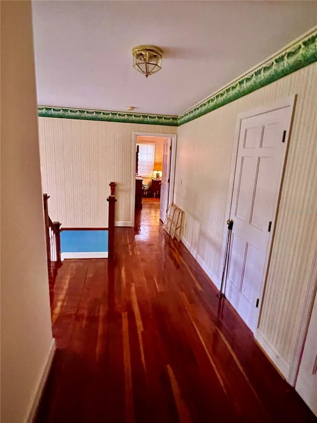 hallway featuring wallpapered walls, baseboards, wood finished floors, and an upstairs landing