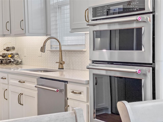 kitchen with stainless steel appliances, tasteful backsplash, sink, and white cabinets