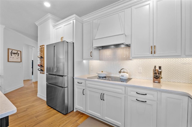 kitchen featuring stainless steel fridge, white cabinets, light wood-type flooring, custom range hood, and crown molding