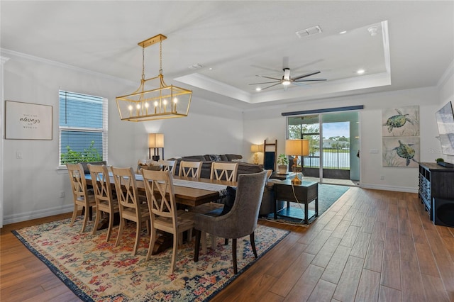 dining space with ornamental molding, a tray ceiling, dark wood-type flooring, and ceiling fan with notable chandelier