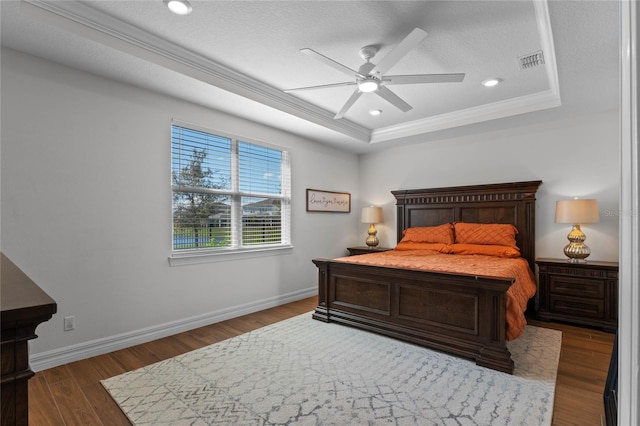 bedroom with ornamental molding, a raised ceiling, dark hardwood / wood-style flooring, a textured ceiling, and ceiling fan