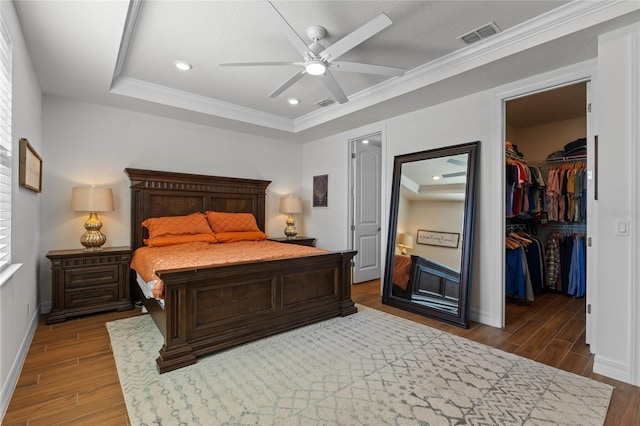 bedroom with ceiling fan, wood-type flooring, ornamental molding, and a walk in closet