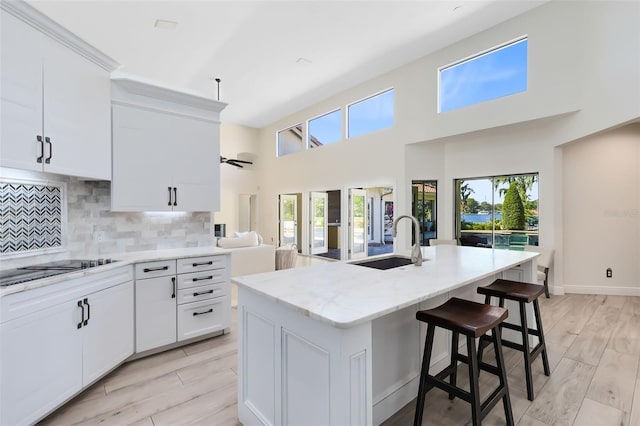 kitchen with a towering ceiling, sink, light hardwood / wood-style floors, white cabinetry, and an island with sink