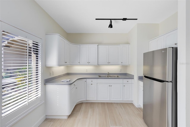 kitchen with track lighting, sink, light hardwood / wood-style flooring, stainless steel fridge, and white cabinetry