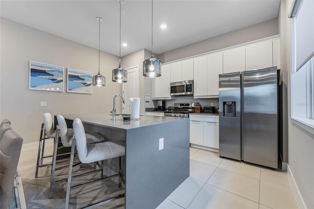 kitchen featuring a kitchen island with sink, sink, appliances with stainless steel finishes, decorative light fixtures, and white cabinetry