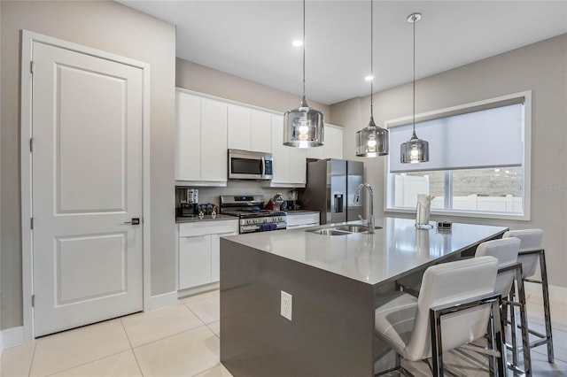 kitchen featuring stainless steel appliances, a kitchen island with sink, sink, decorative light fixtures, and white cabinets