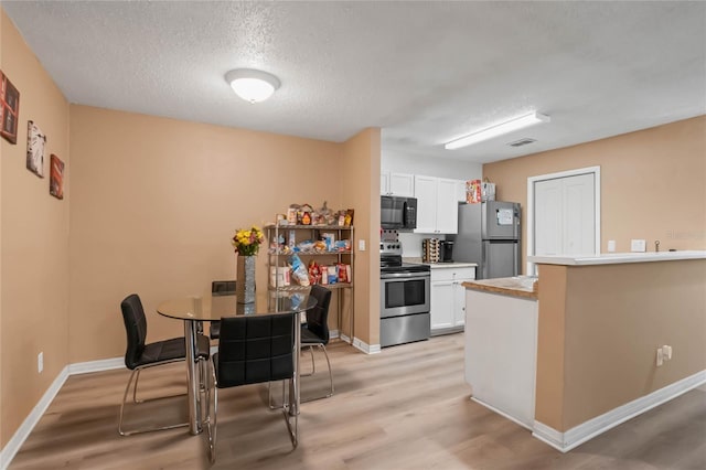 kitchen featuring appliances with stainless steel finishes, white cabinetry, a textured ceiling, and light hardwood / wood-style floors