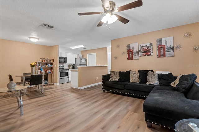 living room featuring a textured ceiling, light wood-type flooring, and ceiling fan