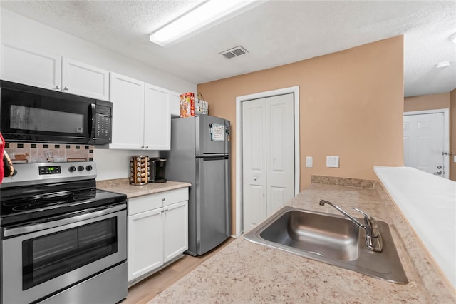 kitchen with white cabinetry, a textured ceiling, light wood-type flooring, sink, and stainless steel appliances