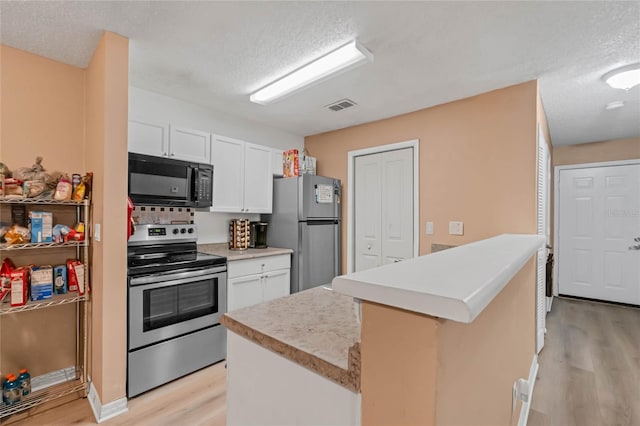 kitchen with appliances with stainless steel finishes, light hardwood / wood-style flooring, white cabinetry, and a kitchen island