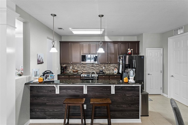 kitchen featuring hanging light fixtures, a breakfast bar area, a textured ceiling, dark brown cabinetry, and stainless steel appliances