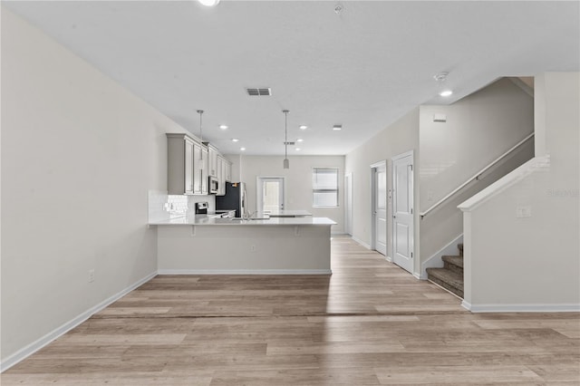 kitchen featuring pendant lighting, kitchen peninsula, appliances with stainless steel finishes, and light hardwood / wood-style floors