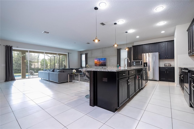 kitchen with stainless steel appliances, a center island with sink, a breakfast bar area, a textured ceiling, and pendant lighting