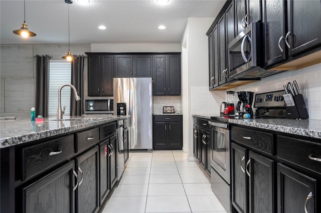 kitchen featuring stainless steel appliances, hanging light fixtures, a textured ceiling, and light stone counters