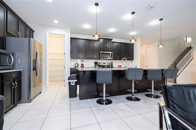 kitchen with appliances with stainless steel finishes, light stone counters, decorative light fixtures, and a breakfast bar