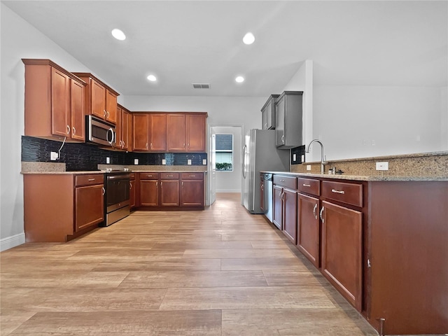 kitchen featuring backsplash, sink, light stone countertops, light wood-type flooring, and appliances with stainless steel finishes