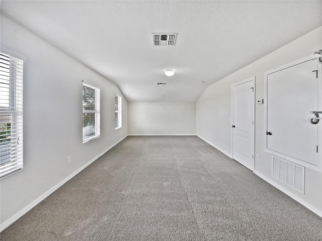 carpeted spare room with a textured ceiling and vaulted ceiling