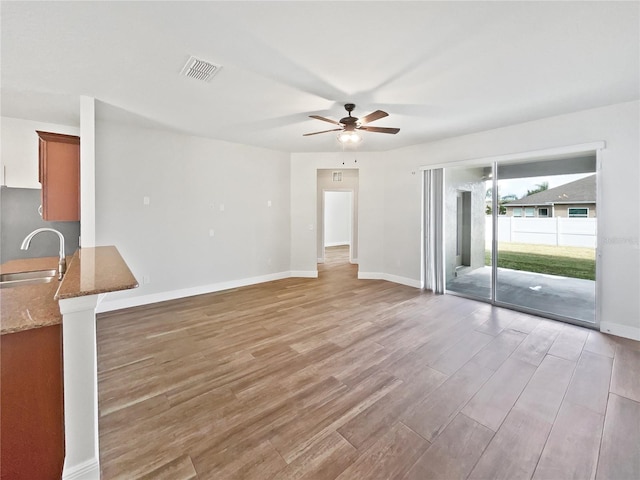 unfurnished living room featuring ceiling fan, sink, and light wood-type flooring