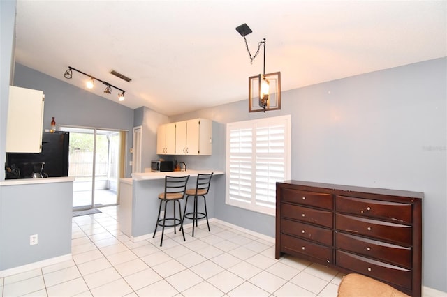 kitchen with kitchen peninsula, black fridge, a kitchen breakfast bar, hanging light fixtures, and light tile patterned floors