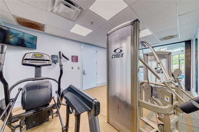 exercise room with a paneled ceiling and light colored carpet