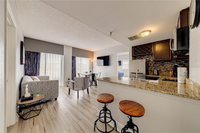 kitchen with light stone countertops, light wood-type flooring, a textured ceiling, and appliances with stainless steel finishes