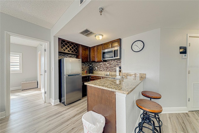 kitchen featuring kitchen peninsula, light stone counters, a textured ceiling, stainless steel appliances, and sink