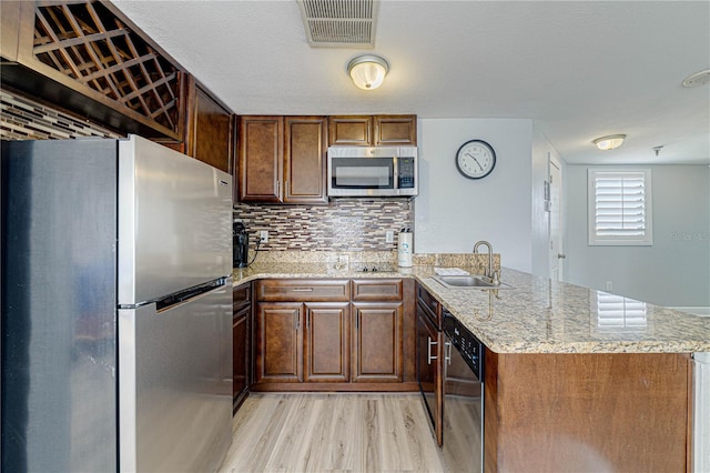 kitchen with sink, light wood-type flooring, appliances with stainless steel finishes, light stone counters, and kitchen peninsula