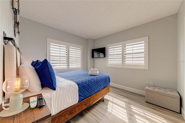 bedroom with a textured ceiling, light hardwood / wood-style floors, and multiple windows