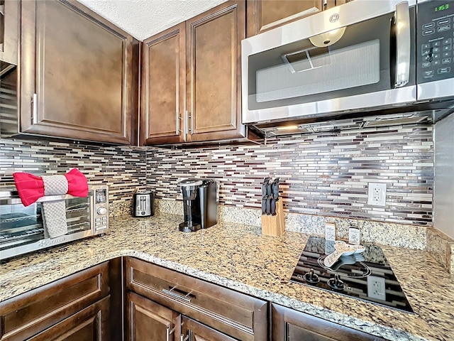 kitchen featuring light stone counters, stainless steel microwave, backsplash, and black cooktop