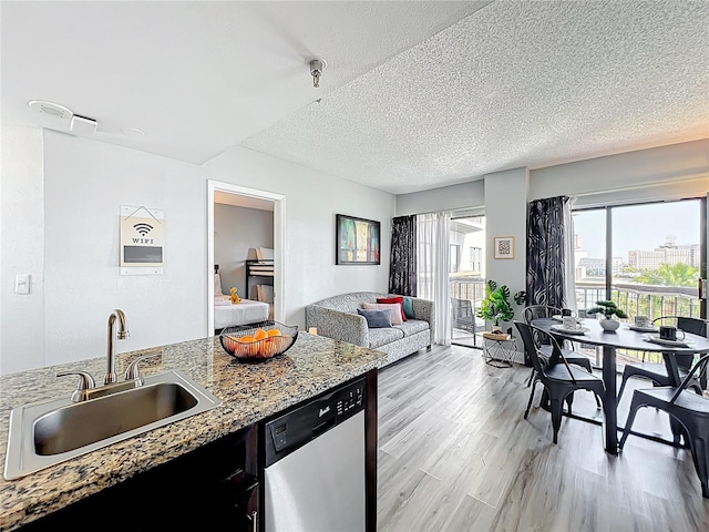 kitchen featuring dishwasher, a sink, open floor plan, light wood-style floors, and a textured ceiling