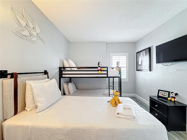 bedroom featuring a textured ceiling, baseboards, and wood finished floors