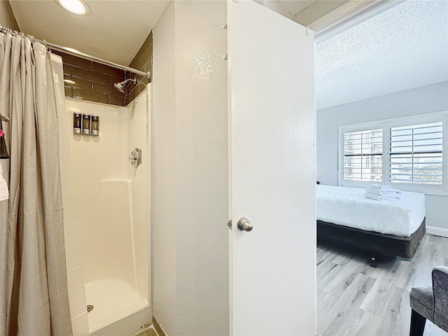 ensuite bathroom featuring baseboards, connected bathroom, a stall shower, and wood finished floors
